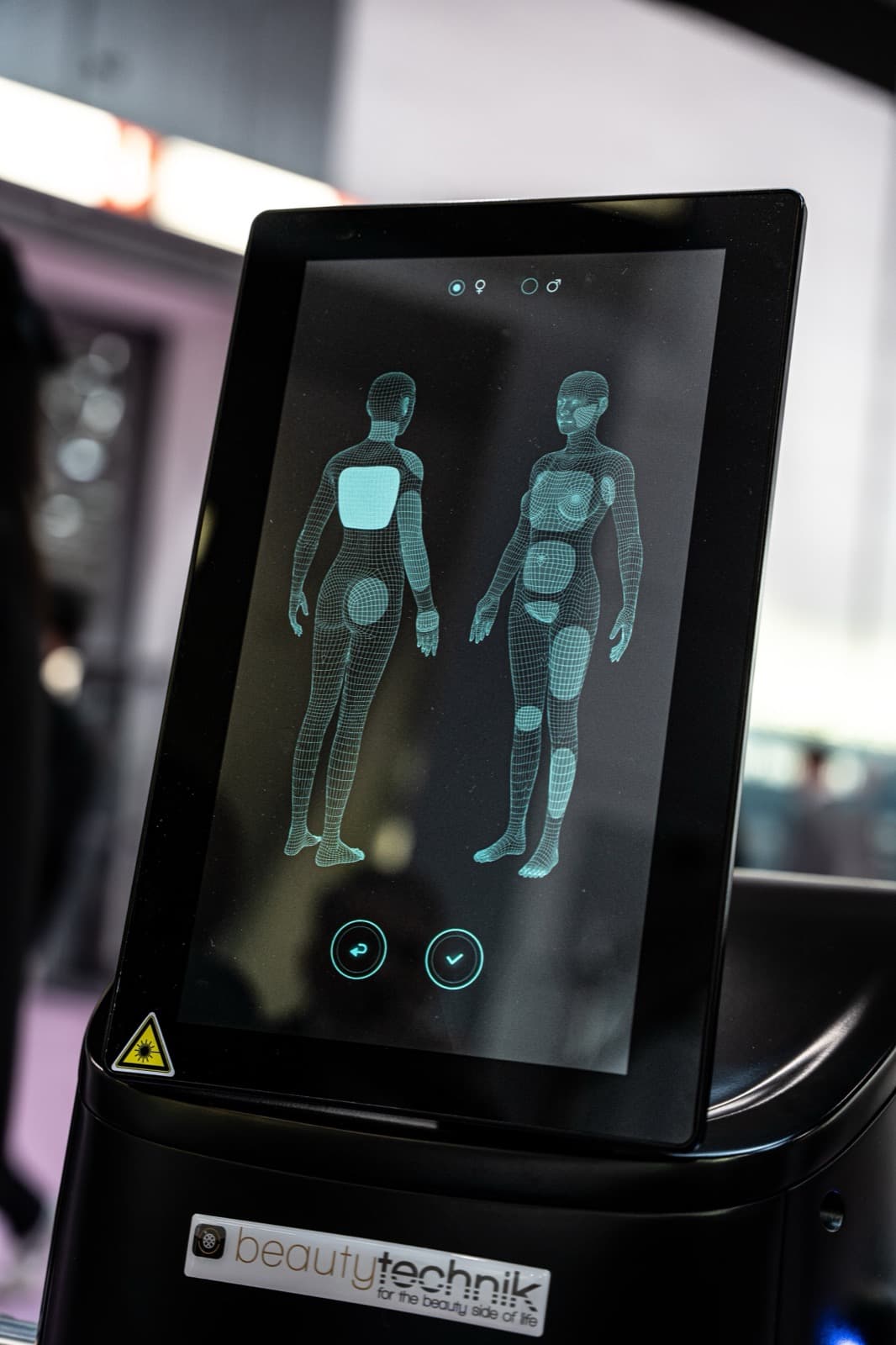 Bildschirm mit 3D-Modellen des menschlichen Körpers zur Auswahl von Behandlungsbereichen.
